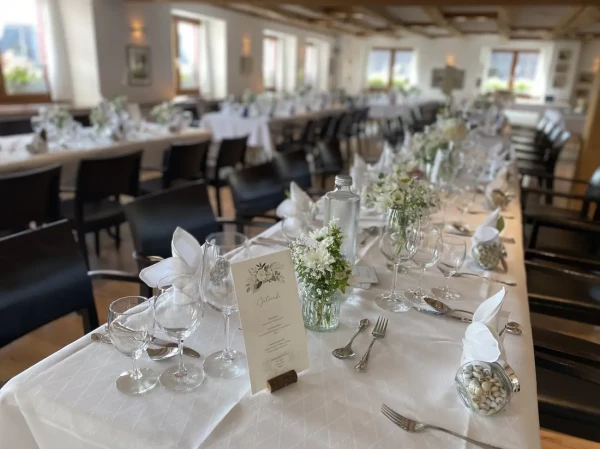 Hochzeitsgedeck mit Menükarte und weißer Blumendekoration. Lange Festtafel mit weisser Tischdecke