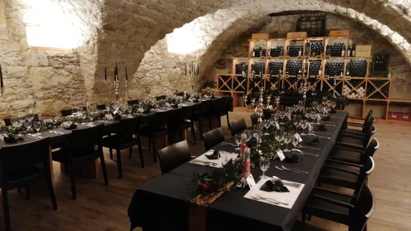 Weinkellerambiente mit schwarzen Tischdecken und festlichem Gedeck. Silberne Kerzenständer und Weinlagerung in traditionellen Holzregalen.