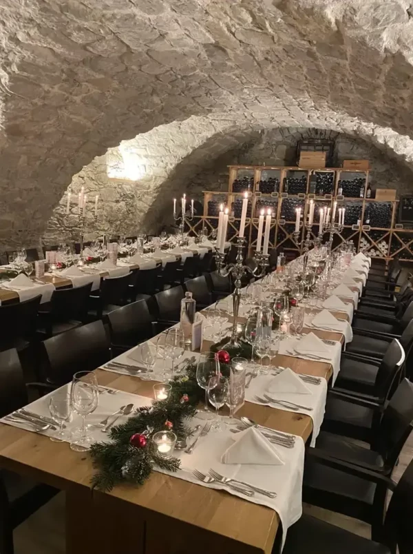 Weihnachtliche Festtafel im Weinkeller mit Tannengrün und Kerzenleuchtern. Stimmungsvolle Beleuchtung unterstreicht die Atmosphäre.