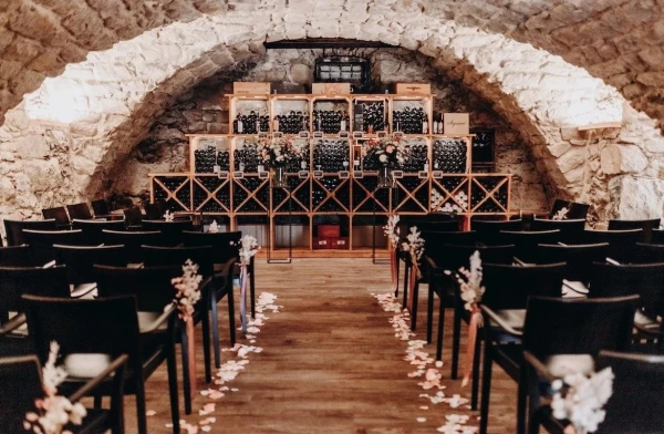 Romantische Trauungslocation mit Blick auf die Weinregale. Stuhlreihen mit Blumengestecken und Rosenblättern dekoriert.