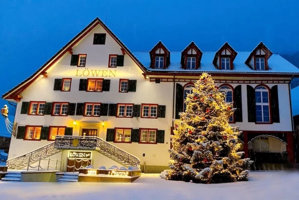 Löwen im Winterkleid mit festlich geschmücktem Weihnachtsbaum. Beleuchtete Fassade in der Abenddämmerung.