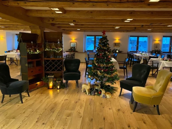 Festlich geschmückter Weihnachtsbaum im Löwen-Saal mit gemütlichen Sesseln in Samt. Rustikale Holzbalkendecke und warme Beleuchtung.