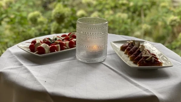 Elegante Appetithäppchen auf weisser Tischwäsche: Caprese-Spieße und gereifter Schinken, dekorativ präsentiert mit Windlicht.