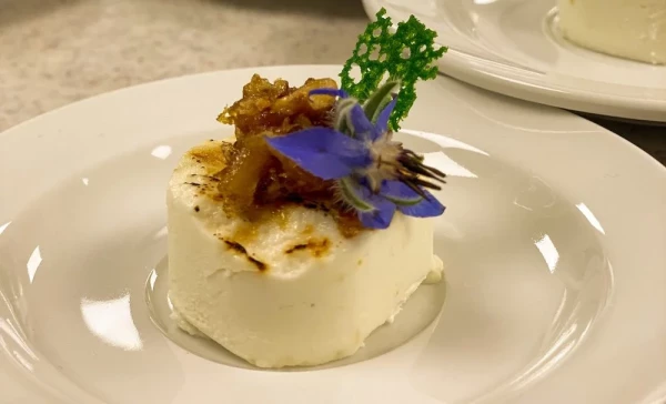 Amuse Bouche aus Ziegenkäse mit karamellisierter Kruste. garniert mit essbarer Borretschblüte und frischen Kräutern