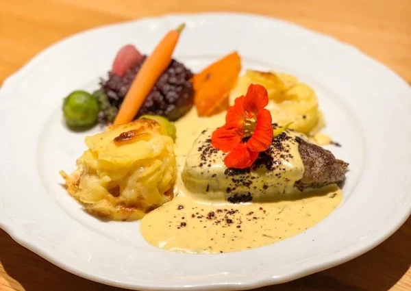 Hauptgang mit zartem Rindsfilet an Sauce Béarnaise, gratiniertem Kartoffelgratin und Gemüse, garniert mit Kapuzinerkresse.