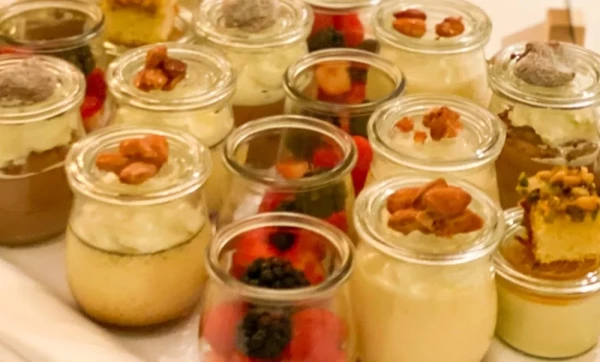 Feine Desserts in kleinen Gläsern, dekoriert mit karamellisierten Nüssen und frischen Beeren.