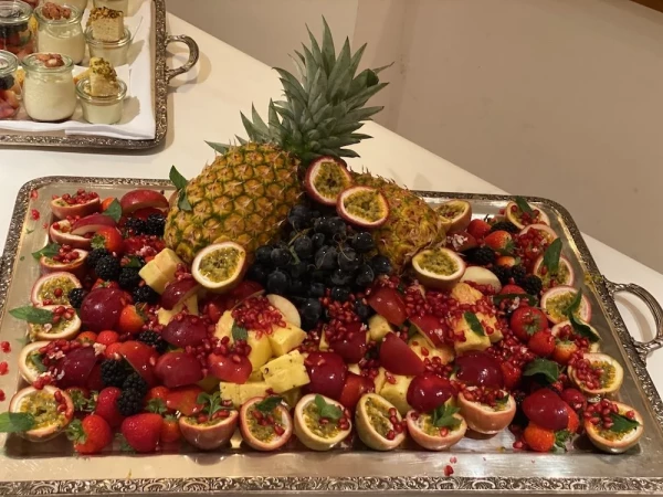 Opulente Obstplatte auf Silbertablett mit Ananas, Passionsfrüchten, Granatapfel und dunklen Trauben. Dekorativ arrangiert mit Beeren.