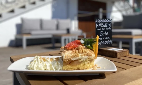 Apfelstreuselkuchen mit Rahm auf der Terrasse vor dem Haus.