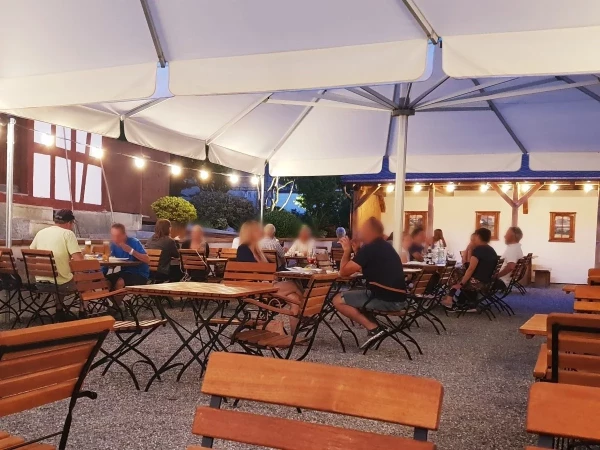 Gemütlicher Biergarten am Abend mit stimmungsvoller Beleuchtung unter weissen Sonnenschirmen