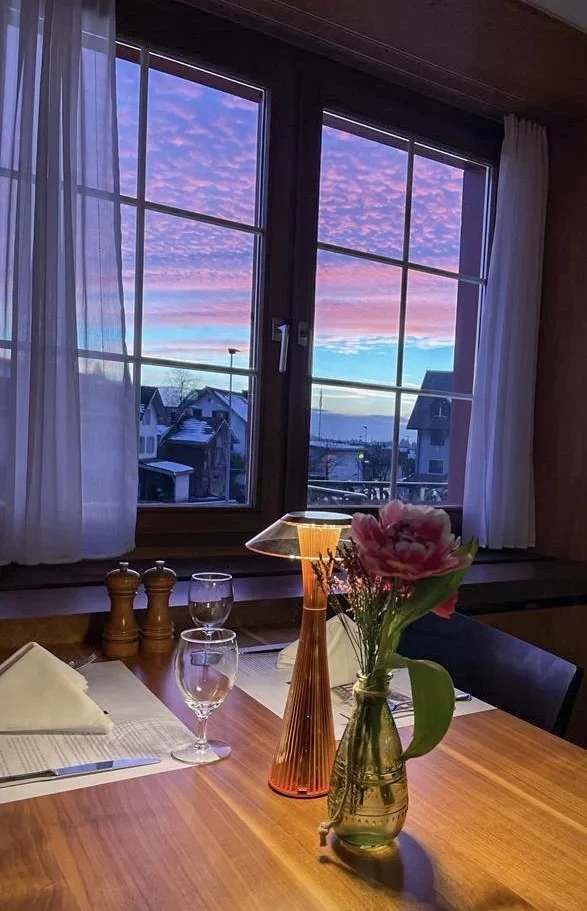 Abendstimmung im gemütlichen Stübli mit spektakulärem rosa-violettem Sonnenuntergang durch das Fenster. 